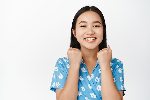 Happy asian woman achieve goal and celebrating winning prize making fist pump and looking enthusiastic standing in dress over white background