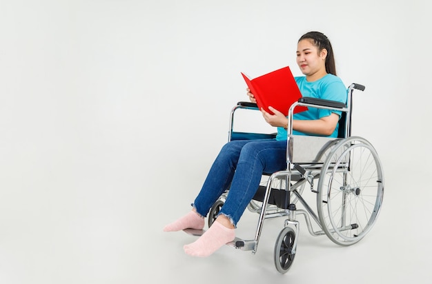 Felice donna asiatica come paziente disabile su sedia a rotelle che legge il rapporto di istruzioni rosso per una sana riabilitazione e guida al trasporto durante il trattamento delle lesioni presso la clinica di riabilitazione e l'ospedale per paralisi.