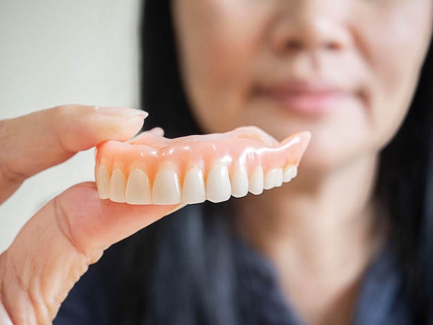 Foto la donna asiatica felice sorride e tiene in mano la dentiera