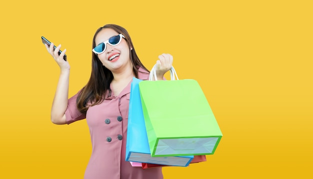 Happy asian woman casual clothes holding credit card and shopping bags on light yellow.