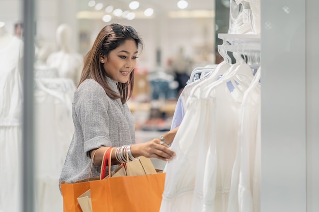 happy asian woman choosing clothes with reflection of glass in store shop with happy actio