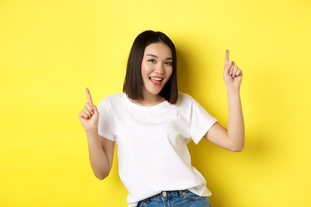 Happy asian woman dancing and having fun, posing in white t-shirt against yellow background.