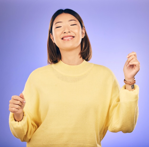 Happy asian woman dancing and music in freedom or casual fashion against a purple studio background female person or model smile enjoying energy event or party in happiness for clothing style