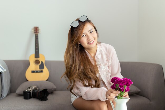 Happy asian woman decorating living room with beautiful flowers at home.