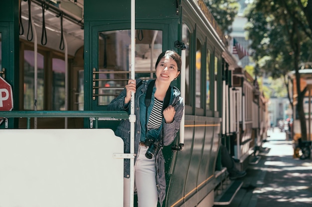 Happy asian woman excited having fun riding popular tourist\
attraction tramway system in san francisco city california during\
summer vacation. tourism lifestyle. female traver smiling on cable\
car