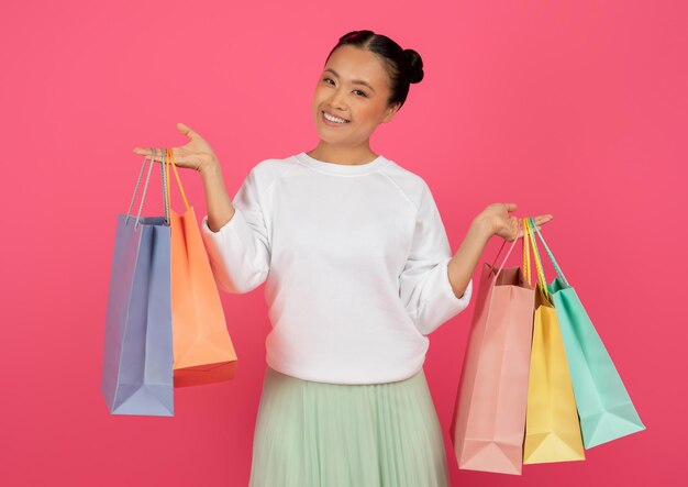 Happy asian woman holding bright paper shopping bags and smiling at camera