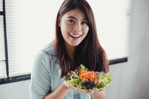 ヘルスケアの笑顔で健康的な食事のための皿野菜を保持している幸せなアジアの女性。新鮮な有機野菜サラダを食べる美しい笑顔の女性。ダイエットコンセプトで健康的なサラダを食べる若い女性。