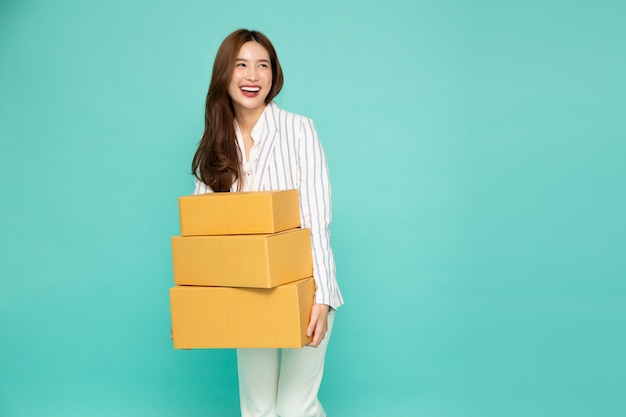 Happy Asian woman holding package parcel box isolated on light green background, Delivery courier and shipping service concept.