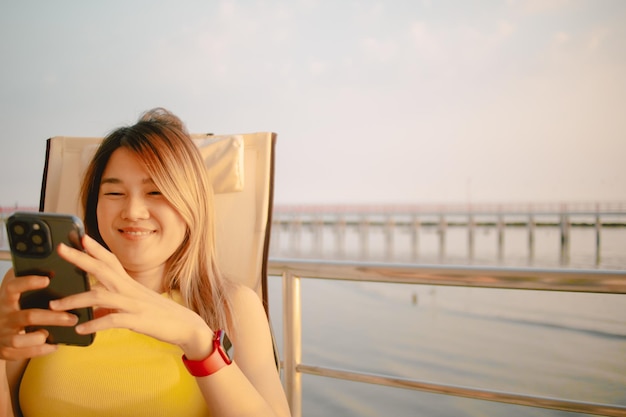 Happy asian woman is reading post in social application on the phone while relaxed her holiday at