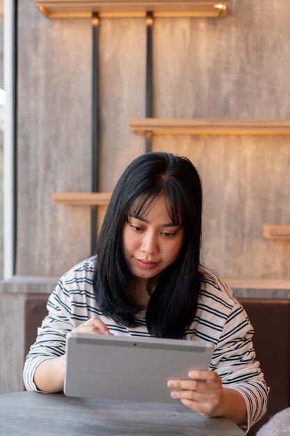 a happy asian woman is using her digital tablet working remotely at a cafe in the city