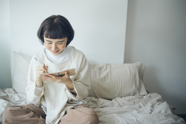 Happy Asian woman is writing at bedroom. She work from home.