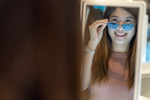 Happy Asian woman looking and choosing eyeglasses in store shop at department store