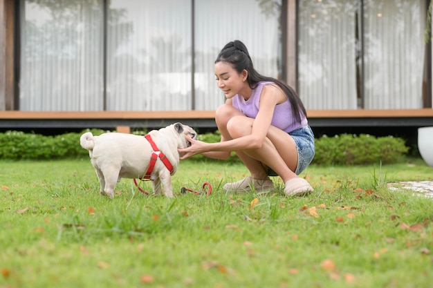 裏庭で可愛い賢いパグ犬と遊ぶ幸せなアジア人女性