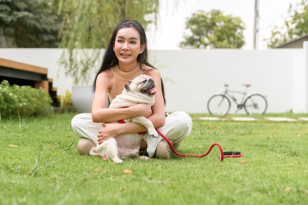 写真 裏庭で可愛い賢いパグ犬と遊ぶ幸せなアジア人女性