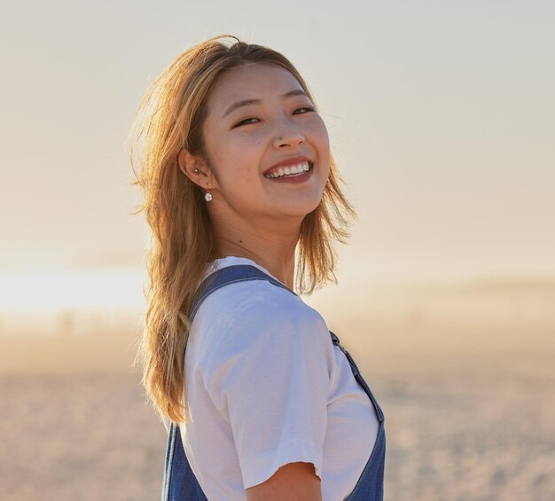 Happy asian woman and portrait smile on the beach for fun travel or vacation trip in the outdoors Japanese female smiling for joyful holiday walk or traveling in happiness by the sandy ocean coast