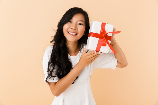 Happy asian woman posing isolated over beige wall space holding gift present box.