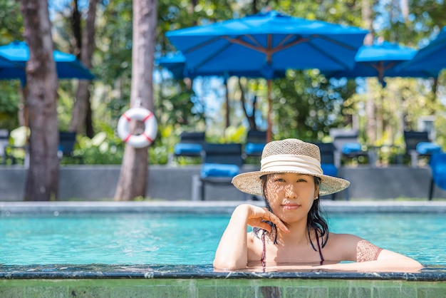 Happy asian woman in red swimsuit and straw hat relax in pool looking at camera at Phangnga Thailand