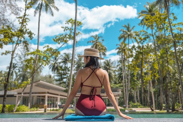 Happy asian woman in red swimsuit and a straw hat relaxing sit by the pool at Phangnga Thailand