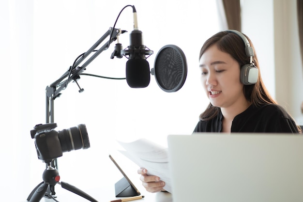 Happy asian woman setting up a living room in her house for\
podcast studio, woman arranging a podcast and online radio station\
at home. professional young podcaster speaking through a\
microphone.