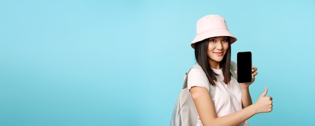 Happy asian woman showing health passport on mobile phone screen vaccinated hand with patch thumbs u