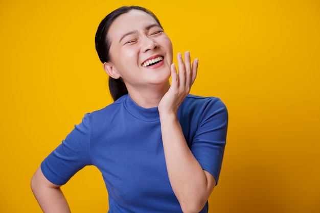 Happy Asian woman showing toothy smile standing over yellow.