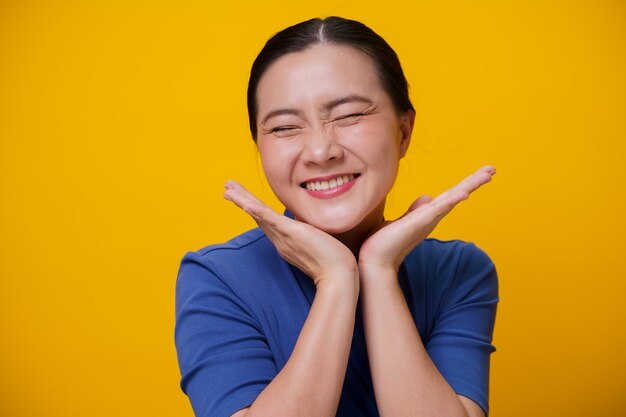 Happy Asian woman showing toothy smile standing over yellow.