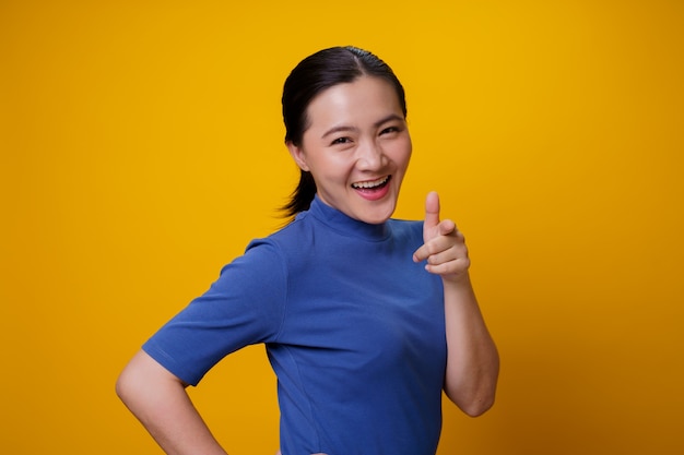 Happy Asian woman showing toothy smile standing over yellow.