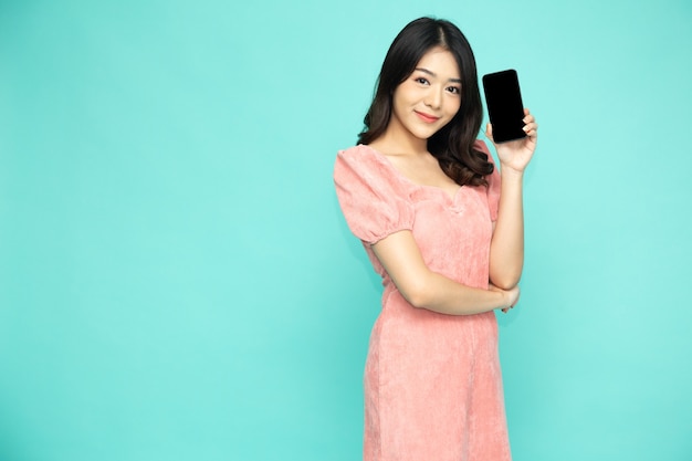 幸せなアジアの女性の笑顔と薄緑の背景に分離された携帯電話を保持します。