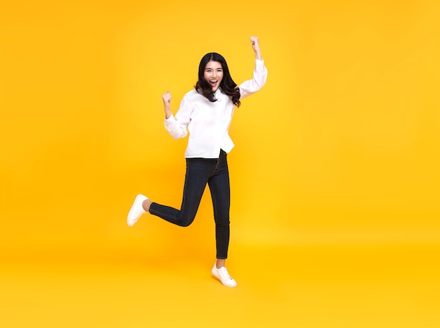 Happy asian woman smiling and jumping while celebrating success isolated over yellow background