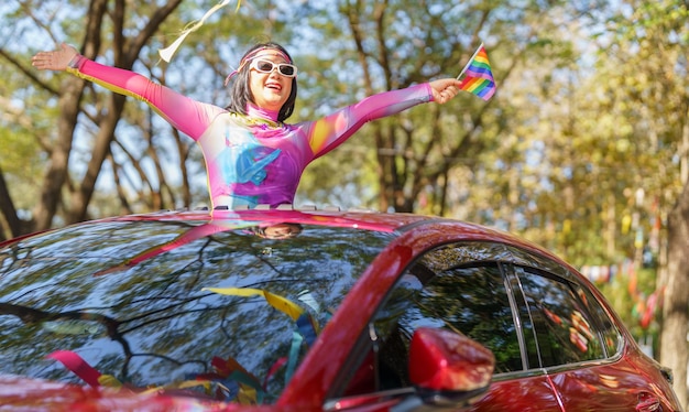 幸せなアジアの女性は、LGBTQ または LGBTQIA の虹で車の中で LGBT プライド パレードをサポートします。