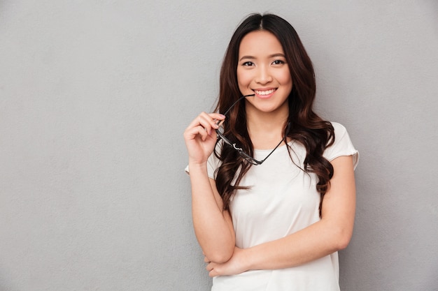 Happy asian woman in t-shirt bites eyeglasses