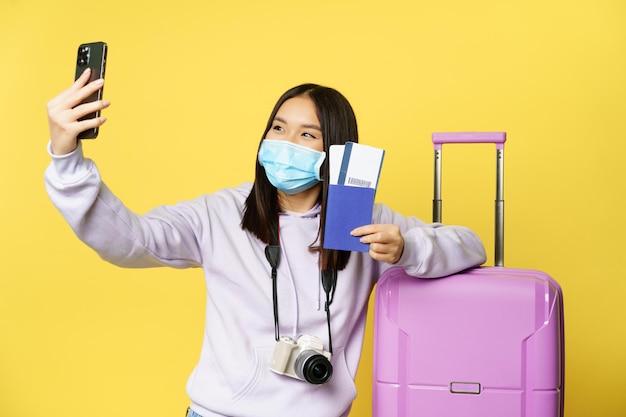 Happy asian woman taking selfie with passport and tickets near suitcase photographing on smartphone ...