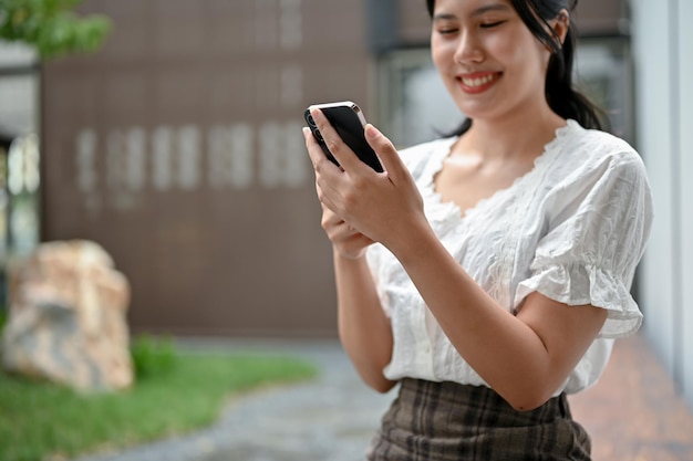 A happy Asian woman using her smartphone while relaxing in the park