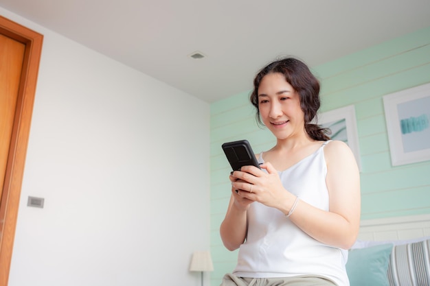 Happy asian woman using mobile phone at home asian housewife\
checking social media holding with smartphone relax woman using\
mobile phone app playing ordering delivery shopping online video\
call