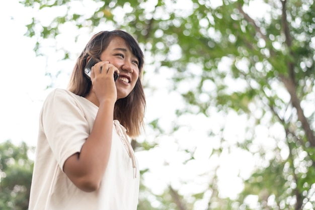 公園でモバイルスマートフォンを使用して幸せなアジアの女性