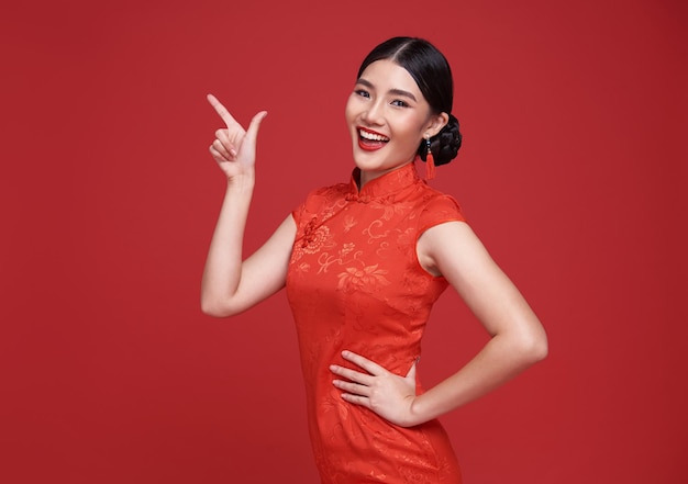 Happy Asian woman wearing traditional cheongsam qipao dress hand pointing up to copy space