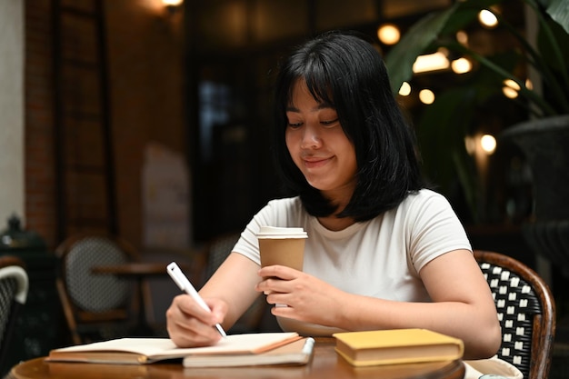 A happy Asian woman working on her tasks on her laptop sitting at a coffee shop