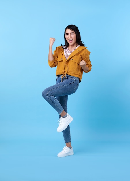 Happy asian woman in yellow shirt having fun and looking at the camera over blue space.