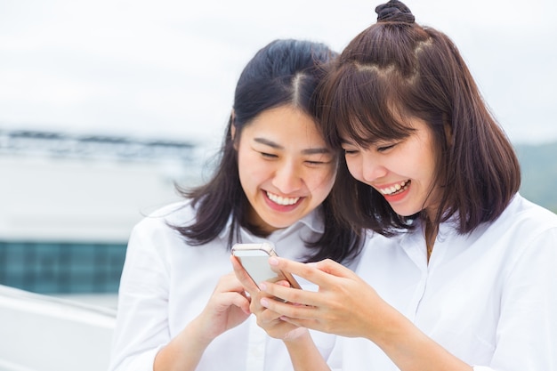 Счастливые азиатские женщины, держащие и использующие свой смартфон для подключения к социальным сетям