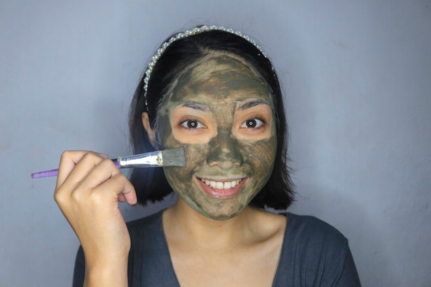 아름다운 얼굴 마스크에 브러시를 사용할 때 웃는 행복한 아시아 여성