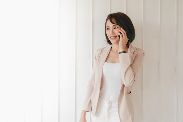 La donna lavoratrice asiatica felice sta avendo una conversazione sullo smartphone