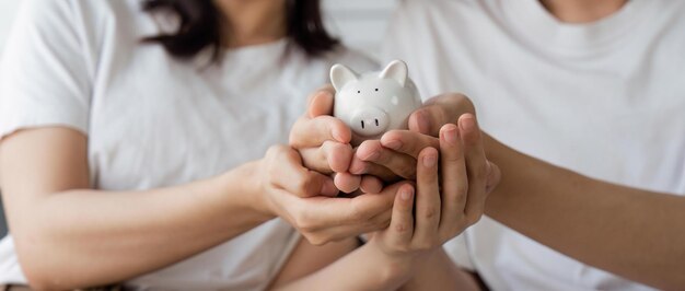 행복한 아시아 젊은 커플은 계산하고 새 집을 위해 부동산을 구입하기 위해 돈을 절약하기 위해 돼지 은행에 동전을 넣는 것을 사랑합니다.