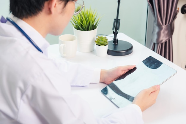 Happy Asian young doctor handsome man smile work from home office wear glasses, using black modern smart digital tablet computer on desk at hospital office, Technology healthcare and medicine concept