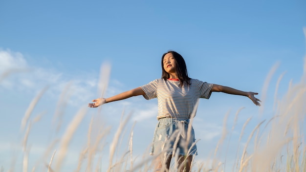 牧草地とblueskyに立っている幸せなアジアの若い女の子。