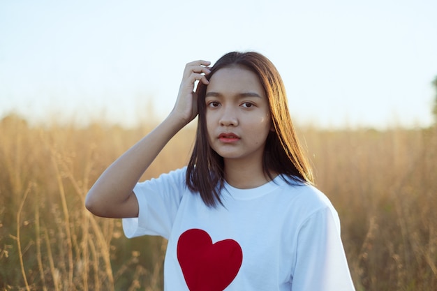 Happy Asian young girl wear white shirt with red heart, hold red paper heart at Meadow on sunset time.