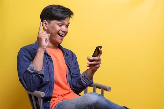 Foto un giovane asiatico felice che tiene il telefono cellulare e sorride ha una nuova idea