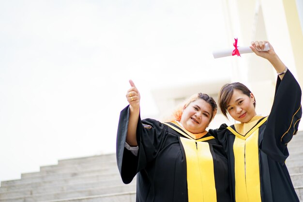 Happy asian young women in the master degree gown showing a\
diploma in their hand close up portrait of confident college\
students in gown in the graduation ceremony