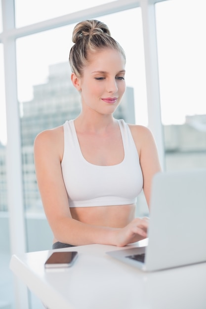 Happy athletic blonde typing on laptop