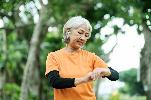 Photo happy athletic senior woman checking her smartwatch in the park