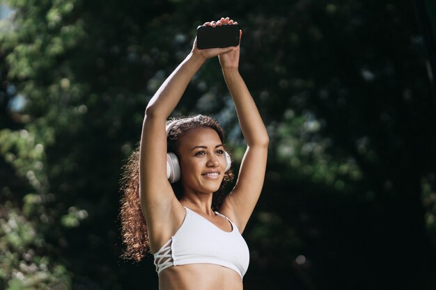 Happy athletic woman in headphones standing in the park